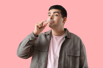 Young man using nasal drops on pink background