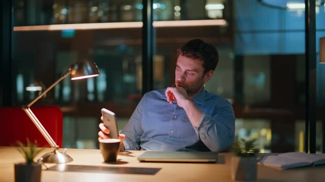 Unmotivated manager checking time phone sitting dark office with coffee closeup.
