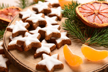 Wooden board of star-shaped gingerbread cookies with mandarin, dried orange and fir branches, closeup