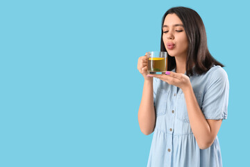 Young woman with glass cup of hot lemon tea on blue background