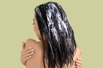Young woman with hair mask on green background, back view