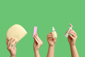 Female hands holding bottles of cuticle oil with cosmetic bag and buffer on green background