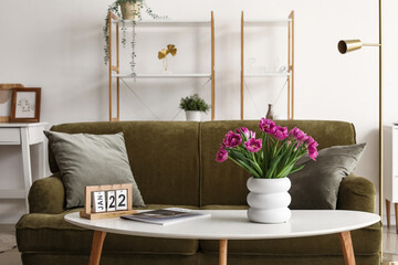 Vase with tulips, magazine and calendar on table in stylish living room interior