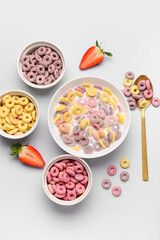 Bowls of colorful sweet cereal rings with milk and cut strawberry on grey background