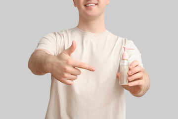 Young man with sanitizer on light background, closeup
