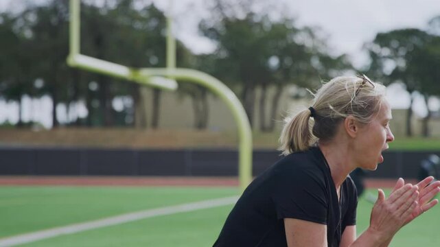A coach blows her whistle and clap her student athletes on during soccer practice