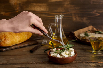 Female hand with fork and bowl of tasty feta cheese and rosemary on wooden background