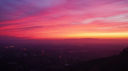A vivid pink and orange sunset casts over a cityscape nestled below mountains.