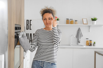 Thoughtful middle-aged woman with red string on her finger baking in kitchen. Reminder concept