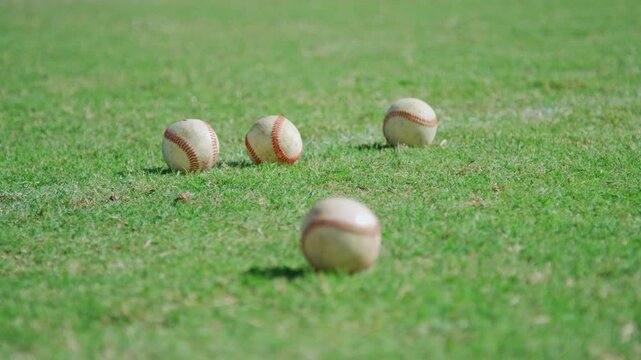 Four baseballs lay on the ground of a high school athletic practice field