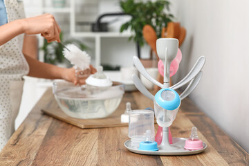 Woman cleaning baby bottle with brush in kitchen, closeup