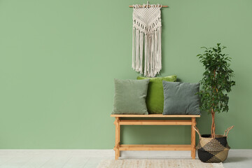 Bench with decorative tree and cushions near green wall in room