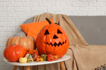 Different Halloween pumpkins on coffee table near white brick wall in room decorated for party