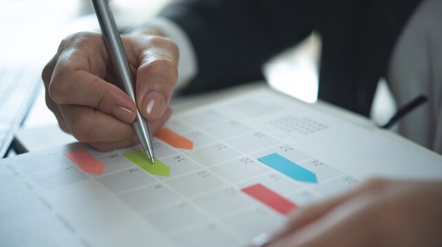 Closeup, woman hand writing on calendar event planner to set timetable organize schedule, event planning for business meeting or vacation plan. Organization and business planning concept.