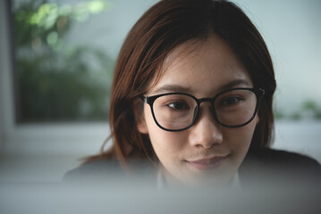 Closeup, asian business woman with eyeglasses working on computer, looking at the computer monitor screen at office