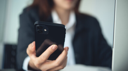 Closeup, businesswoman using mobile phone, working on laptop computer at office. Business woman hand with phone for working online on computer device for research in office, business background