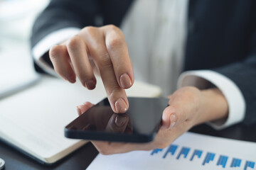 Closeup, businesswoman hand using mobile phone with business document, financial report on office table. Business woman using smartphone to calculate business data, working at office