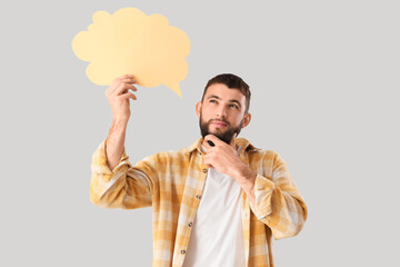 Handsome young thoughtful man with blank speech bubble on grey background