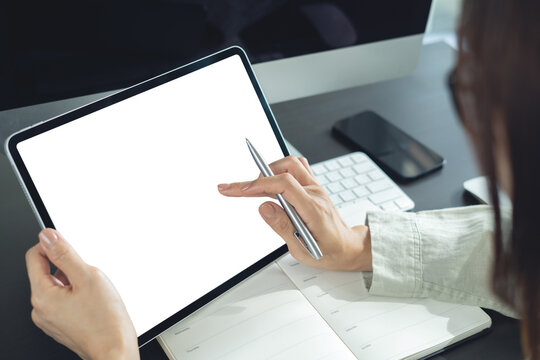 Mockup, using digital tablet with blank screen. Business woman using digital tablet at office, finger touching on blank screen with calendar planner notebook and computer on table