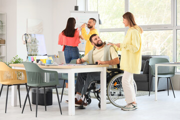 Male designer in wheelchair working with graphic tablet and colleague at office