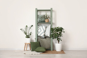 Shelving unit with pillows and houseplants near white wall in room