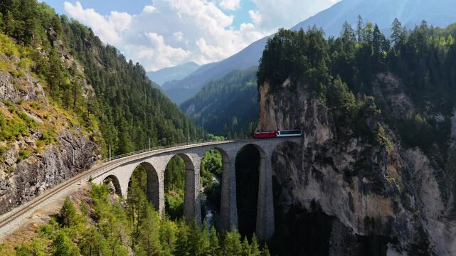 Drone footage of a train emerging from a tunnel and crossing the iconic Landwasser Viaduct in the Swiss Alps