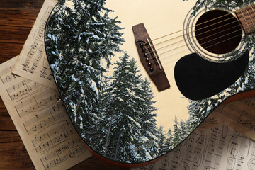 Guitar and music sheets on wooden table, top view. Musical instrument and snowy coniferous trees,...