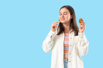Young woman eating cookies on blue background
