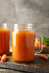 Fresh carrot juice in mason jars and vegetables on wooden table against gray background