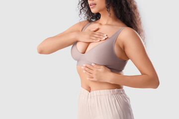 Young African-American woman checking her breast on light background, closeup. Cancer awareness...
