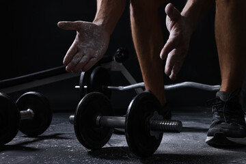 Man clapping hands with talcum powder before training with barbells on black background, closeup
