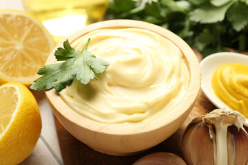 Delicious mayonnaise sauce with parsley in bowl, lemon and garlic on table, closeup