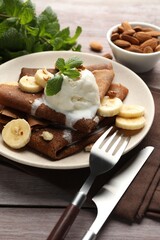 Delicious chocolate crepes with banana, nuts, mint and scoop of ice cream on wooden table, closeup