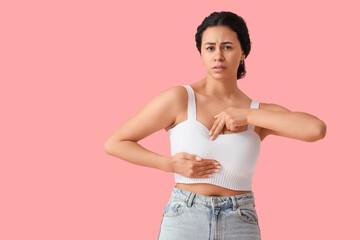Worried African-American woman checking her breast on pink background. Cancer awareness concept