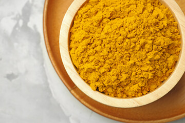 Turmeric powder in bowl on light grey table, top view