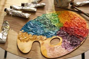 Wooden palette with bright paints, brush and tubes on table, closeup