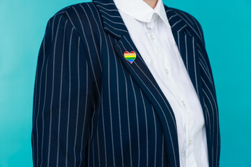 Woman with heart shaped pin in LGBT colors on light blue background, closeup