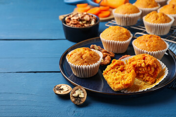 Tasty carrot muffins and walnuts on blue wooden table, closeup. Space for text