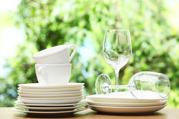 Different clean dishware, cups and glasses on wooden table against blurred green background
