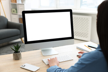 Woman looking at monitor with blank screen at wooden table indoors. Mockup for design