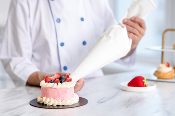 Confectioner with pastry bag making cake at marble table in kitchen, selective focus