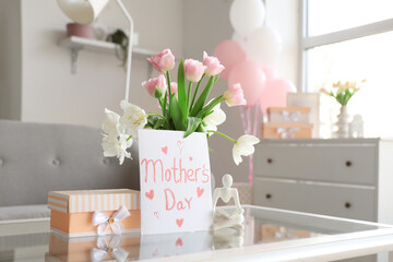 Card for Mother's Day with flowers and gift box on table in living room