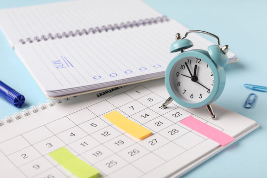 Calendar with alarm clock and notebook with todo list on blue background, closeup