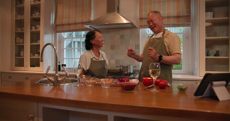 In kitchen, Senior Asian couple dancing surrounded by cooking ingredients and tablet, at home - Powered by Adobe