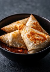 Crispy samosas served in a bowl with dipping sauce.
