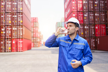 Caucasian white container yard worker takes a break to drink a water from bottle in very hot day.