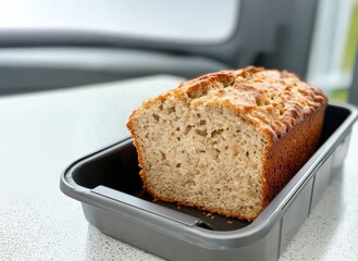 A freshly baked loaf of bread sits in a black baking pan, showcasing its golden crust and soft interior.