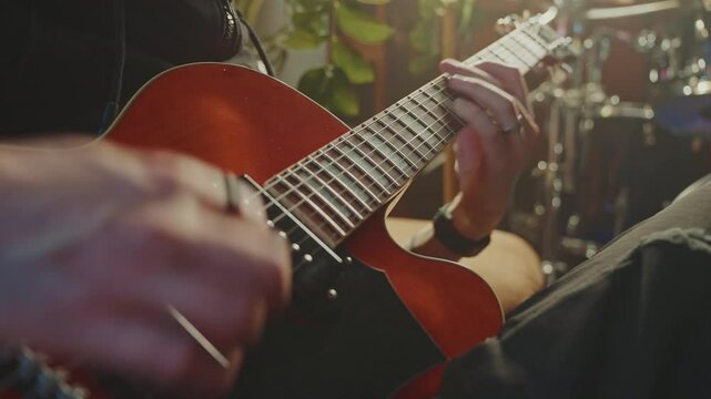 Concentrated guitarist performing melodic riffs on vibrant red electric guitar within professional recording studio, surrounded by comprehensive musical equipment and instruments