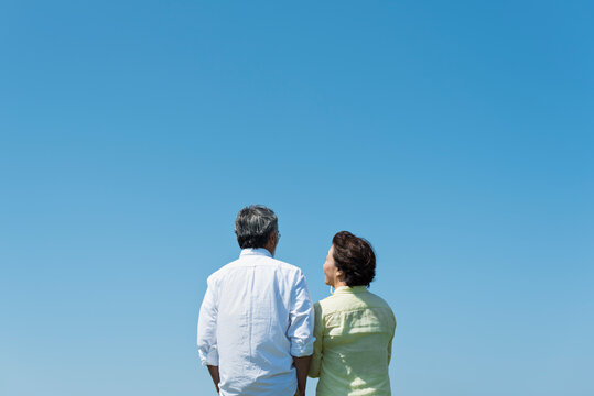 青空の下で寄り添い合うシニア夫婦