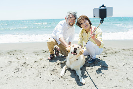 海辺で愛犬と写真を撮るシニア夫婦